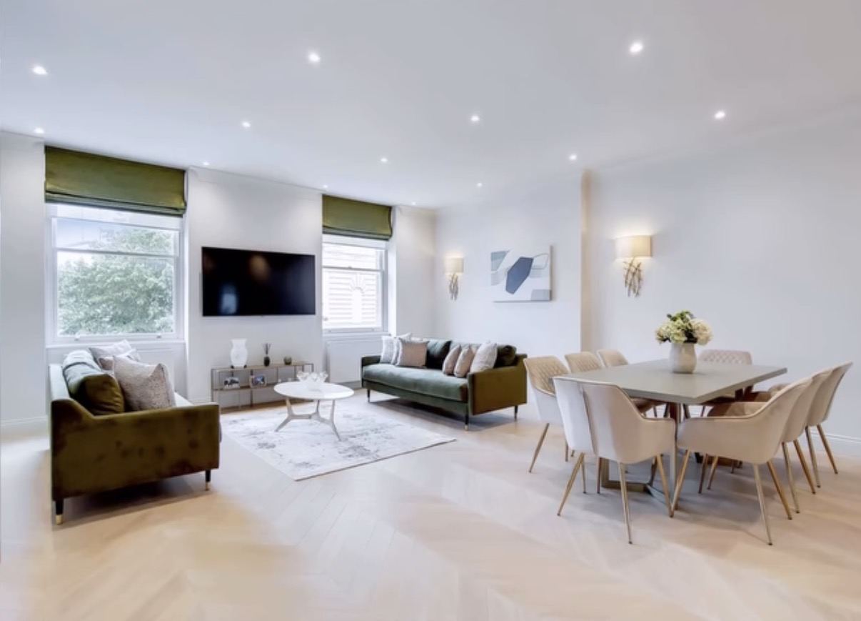 Open-plan living and dining room with herringbone floor, green sofas and a set dining table