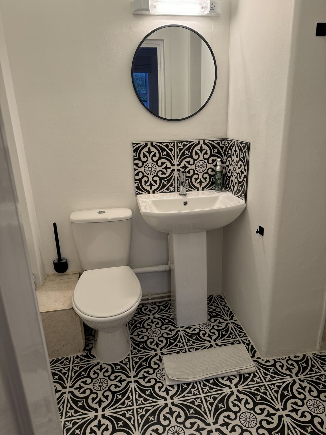 Shower room with patterned black and white floor tiles and round mirror